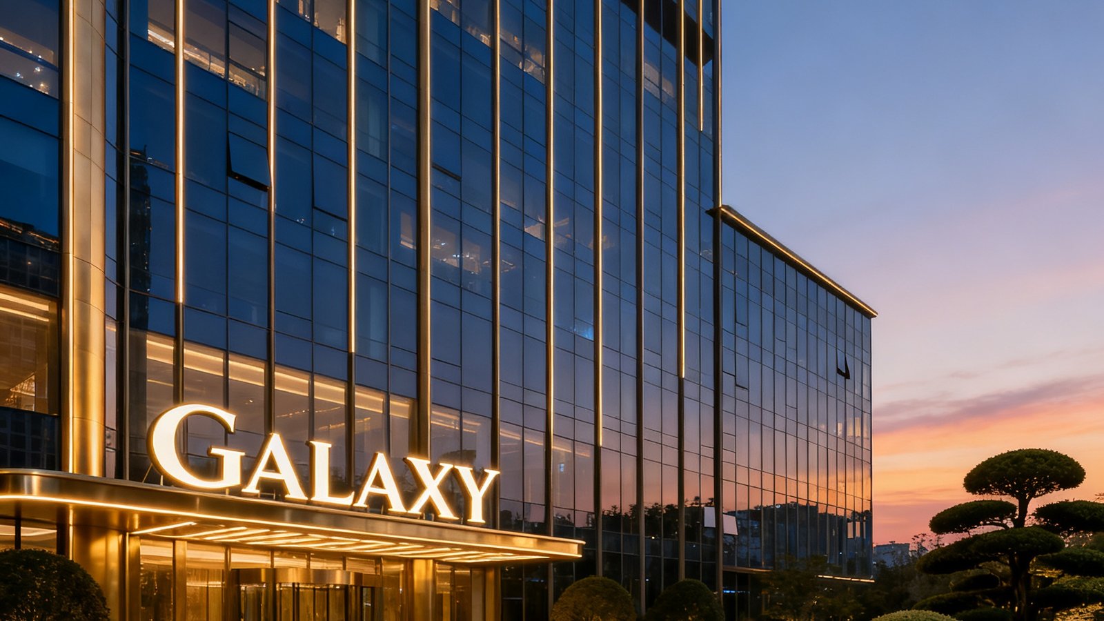 银河贵宾汇GALAXY总部所在的超甲级写字楼外立面，建筑采用玻璃幕墙与金属线条结合的设计，楼顶GALAXY标识在傍晚天色中熠熠生辉，周边环绕着精心修剪的绿植景观。